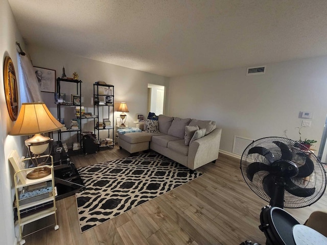 living area with visible vents, a textured ceiling, and wood finished floors