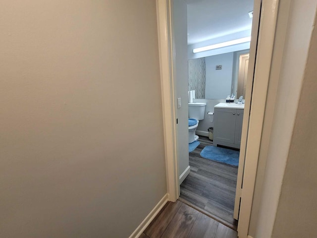 hall with dark wood-type flooring, baseboards, and a sink