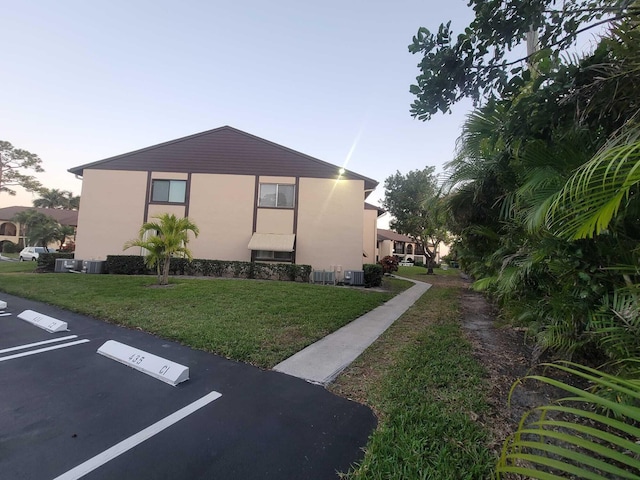 view of side of property with uncovered parking, a lawn, and stucco siding