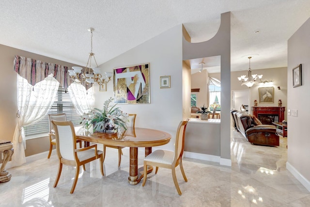 dining room featuring a notable chandelier, a glass covered fireplace, vaulted ceiling, a textured ceiling, and baseboards