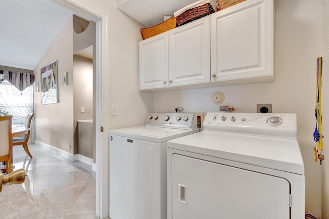 laundry area with washing machine and dryer, cabinet space, a textured ceiling, and baseboards