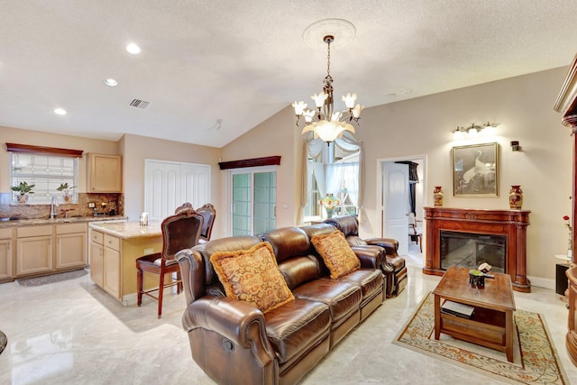 living room featuring visible vents, an inviting chandelier, a glass covered fireplace, vaulted ceiling, and a textured ceiling