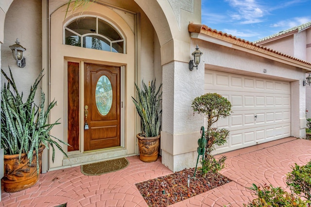 view of exterior entry with a garage, a tiled roof, and stucco siding