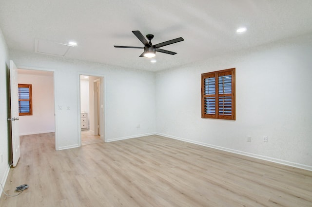 spare room featuring light wood-type flooring, attic access, baseboards, and a ceiling fan