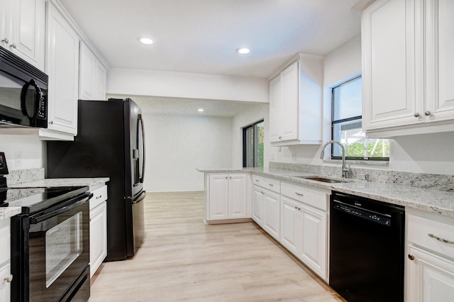 kitchen with light wood finished floors, white cabinets, a peninsula, black appliances, and a sink