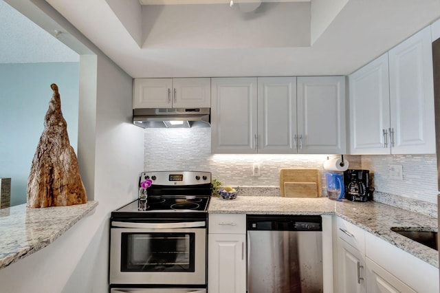 kitchen featuring under cabinet range hood, white cabinetry, appliances with stainless steel finishes, decorative backsplash, and light stone countertops