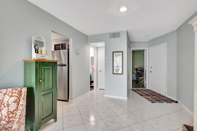 entrance foyer with light tile patterned floors, a textured ceiling, visible vents, and baseboards