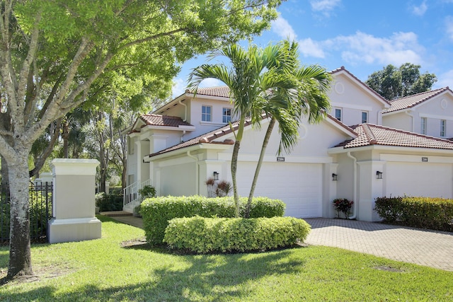 mediterranean / spanish home with an attached garage, a tiled roof, decorative driveway, stucco siding, and a front yard