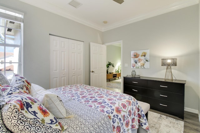 bedroom with wood finished floors, visible vents, baseboards, ornamental molding, and a closet