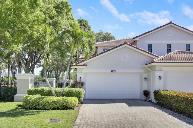 mediterranean / spanish home with an attached garage, fence, a tiled roof, decorative driveway, and stucco siding