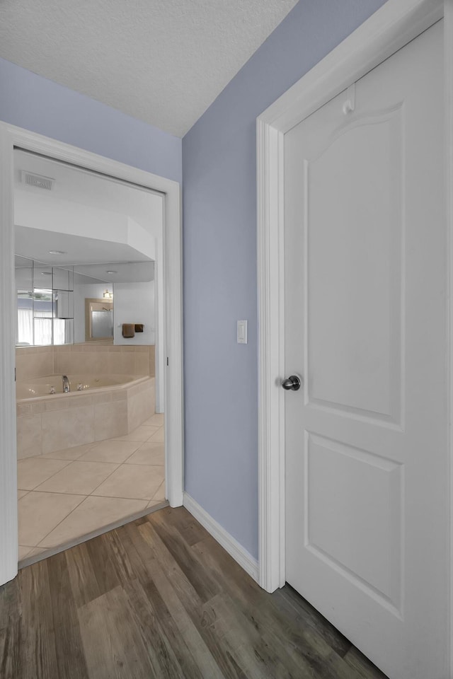 interior space with a textured ceiling, a garden tub, wood finished floors, visible vents, and baseboards