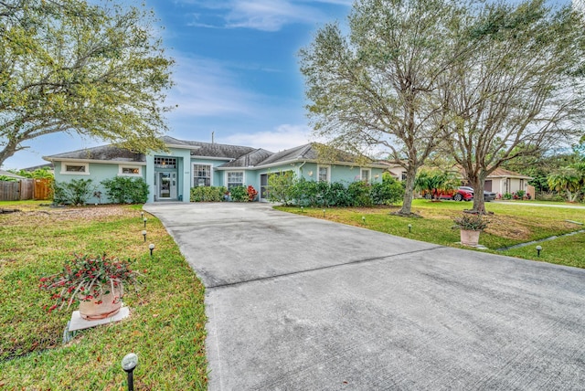 ranch-style house with driveway, fence, a front lawn, and stucco siding