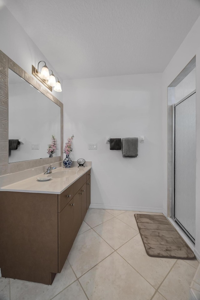 bathroom with a shower with door, vanity, a textured ceiling, baseboards, and tile patterned floors