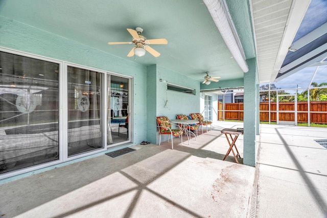 view of patio featuring glass enclosure, fence, and a ceiling fan