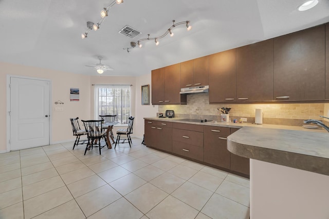 kitchen with light tile patterned floors, black electric cooktop, under cabinet range hood, visible vents, and decorative backsplash