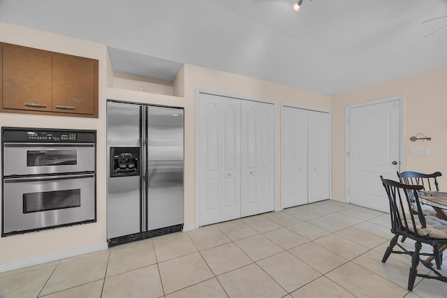 kitchen featuring brown cabinets, lofted ceiling, stainless steel appliances, and light tile patterned flooring