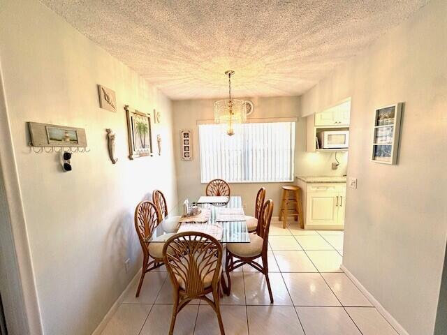 dining room with a textured ceiling, light tile patterned floors, baseboards, and a chandelier