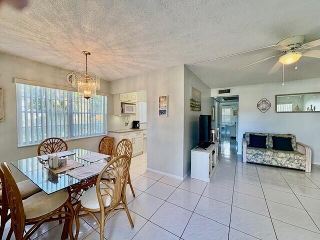 dining space featuring visible vents, baseboards, light tile patterned floors, ceiling fan with notable chandelier, and a textured ceiling