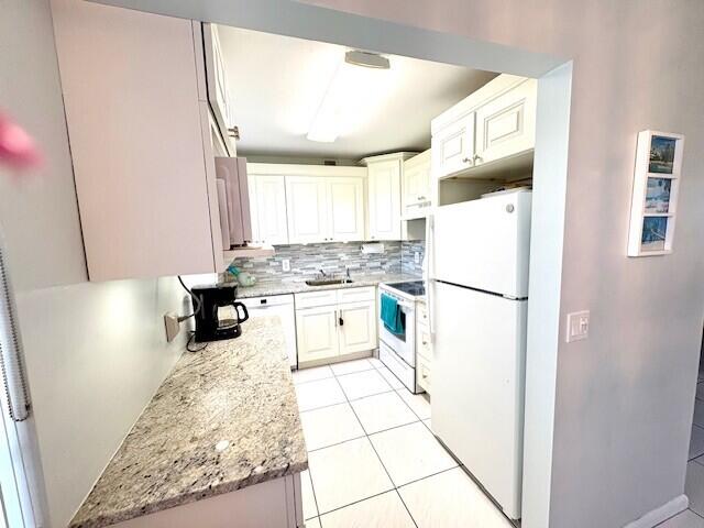 kitchen with white appliances, light stone counters, light tile patterned floors, a sink, and decorative backsplash