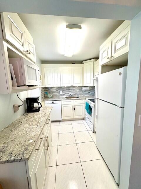 kitchen with white appliances, light stone counters, light tile patterned flooring, a sink, and backsplash