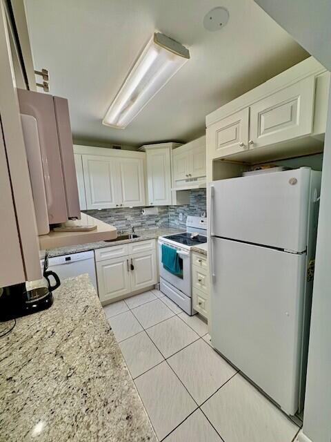 kitchen featuring tasteful backsplash, under cabinet range hood, light tile patterned floors, white cabinets, and white appliances