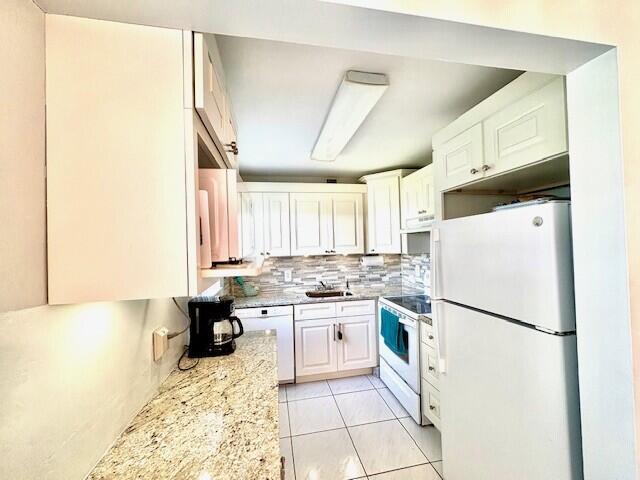 kitchen featuring a sink, white cabinetry, white appliances, light tile patterned floors, and decorative backsplash