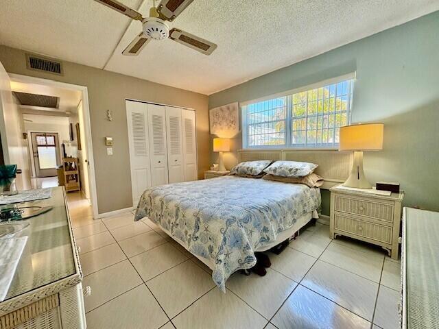 bedroom with a closet, visible vents, a textured ceiling, and light tile patterned flooring