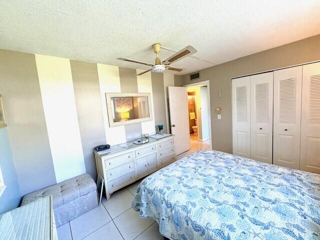 bedroom with visible vents, a textured ceiling, a closet, light tile patterned floors, and ceiling fan