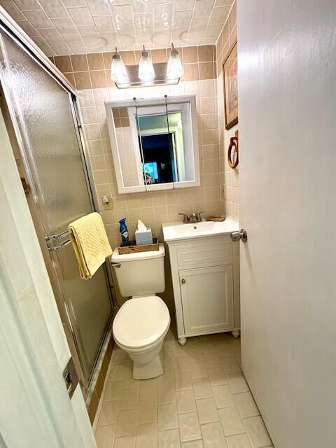 bathroom featuring toilet, vanity, a stall shower, tile patterned floors, and tile walls