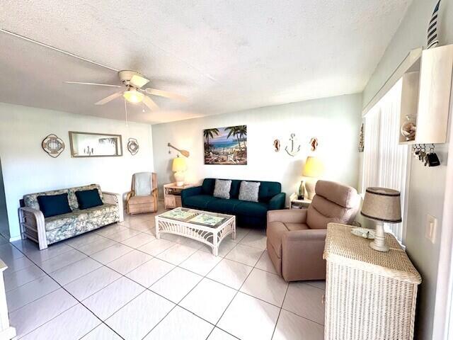 living room featuring a textured ceiling, light tile patterned floors, and ceiling fan