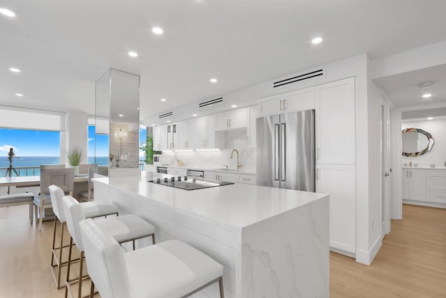 kitchen featuring white cabinets, a kitchen island, high end fridge, black electric cooktop, and a sink