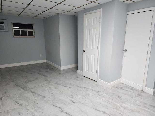 finished basement with a paneled ceiling, marble finish floor, a wall mounted air conditioner, and baseboards