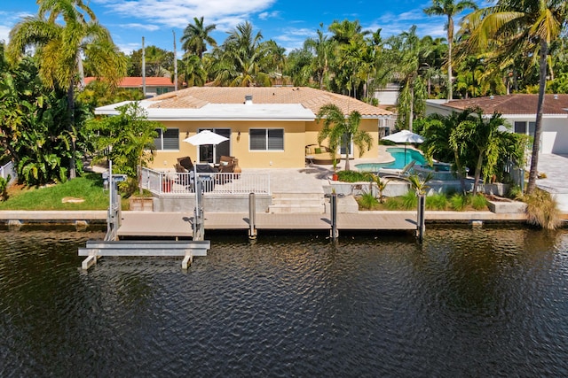 rear view of property featuring an outdoor pool, stucco siding, a water view, and a patio area