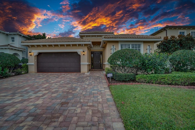 mediterranean / spanish home with an attached garage, a tiled roof, decorative driveway, and stucco siding