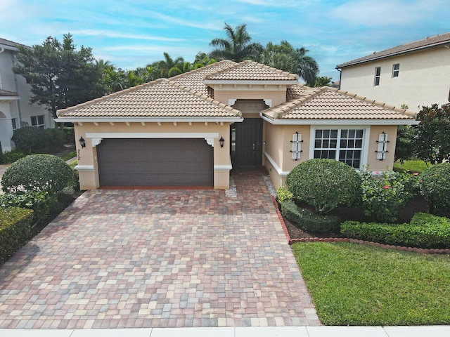 view of front facade with decorative driveway, a tile roof, an attached garage, and stucco siding