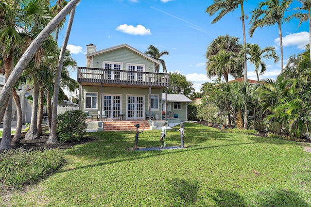 back of property with a chimney, a lawn, and french doors