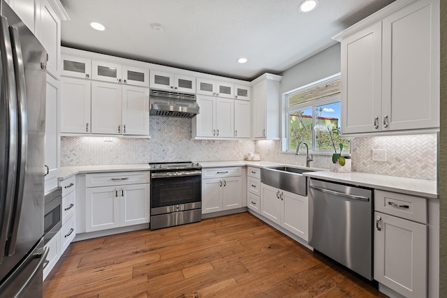 kitchen featuring hardwood / wood-style floors, stainless steel appliances, light countertops, under cabinet range hood, and a sink