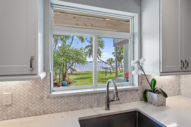 kitchen with backsplash, a sink, and light stone countertops