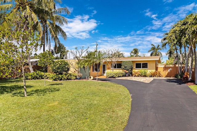 ranch-style house with a front yard, driveway, fence, and stucco siding