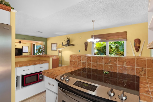 kitchen with appliances with stainless steel finishes, tile counters, white cabinets, and a textured ceiling