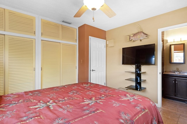 tiled bedroom with two closets, visible vents, ensuite bathroom, a ceiling fan, and a sink