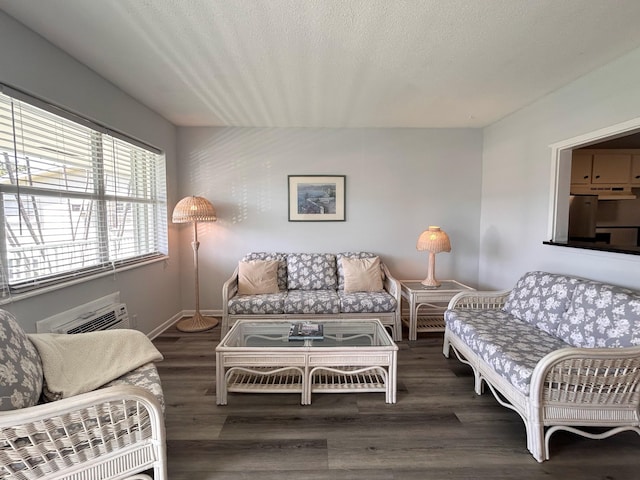 living area featuring a textured ceiling, an AC wall unit, wood finished floors, and baseboards