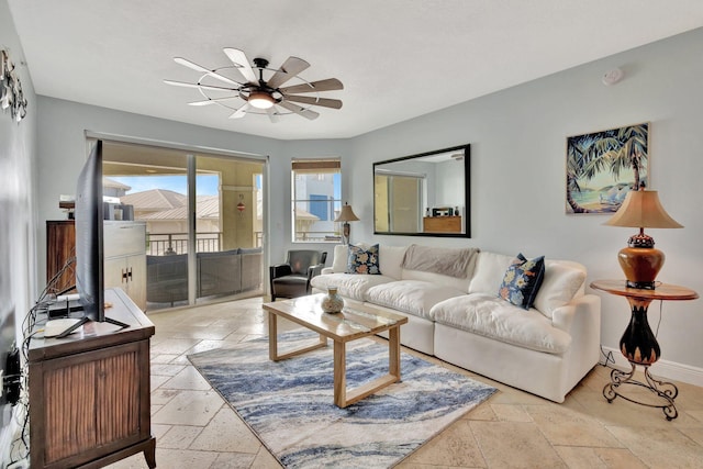 living area featuring stone tile floors, baseboards, ceiling fan, and a textured ceiling