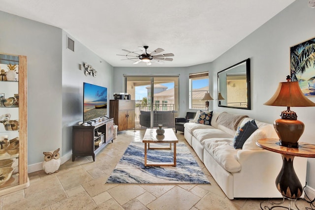 living area with baseboards, ceiling fan, visible vents, and stone tile floors