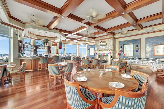 dining area with beam ceiling, ornamental molding, a large fireplace, wood finished floors, and coffered ceiling