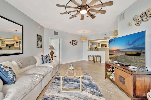 living room featuring ceiling fan, visible vents, baseboards, and stone finish flooring