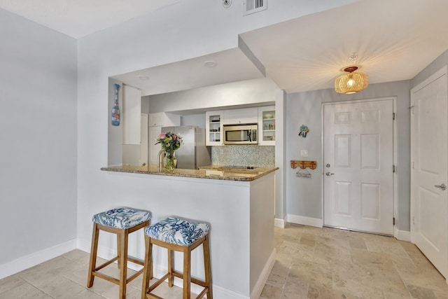 kitchen with stone counters, stainless steel appliances, visible vents, decorative backsplash, and white cabinetry