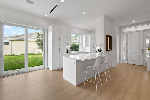 kitchen featuring visible vents, light wood finished floors, a kitchen breakfast bar, and white cabinetry