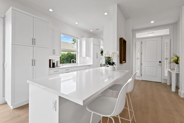 kitchen featuring light wood-type flooring, a breakfast bar, white cabinets, and a sink