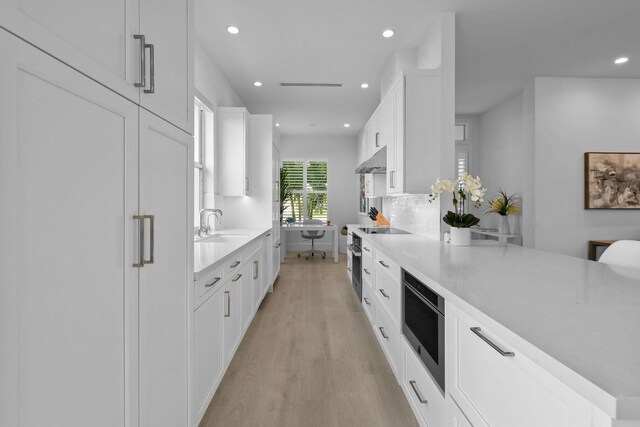 kitchen featuring recessed lighting, backsplash, light wood-style floors, a sink, and under cabinet range hood